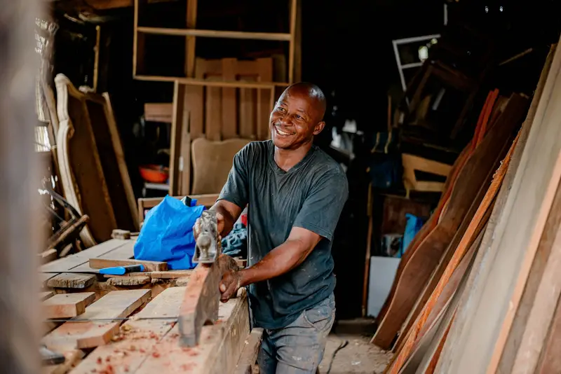 Carpenter smiling as he planes a plank of wood