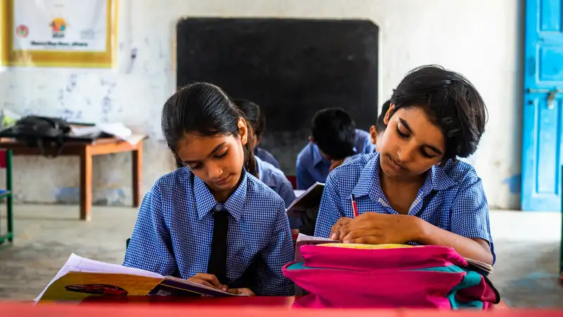 Two schoolgirls writing in their notebooks in class